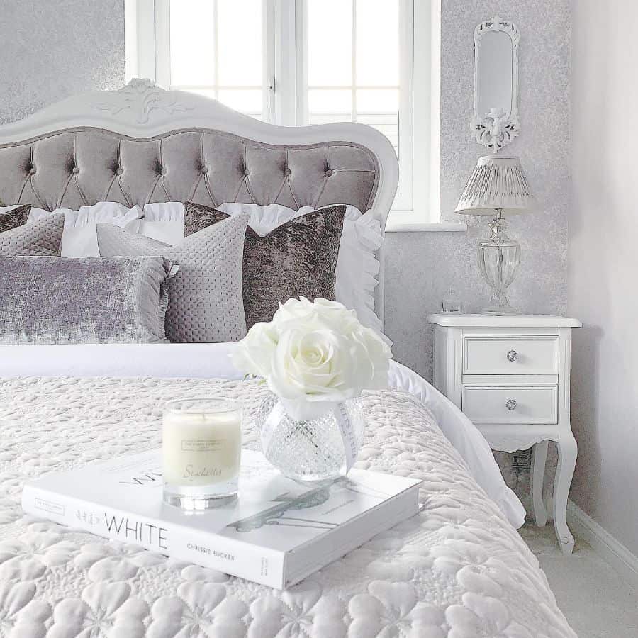 Elegant bedroom with tufted headboard, decorative pillows, and white roses on nightstand.