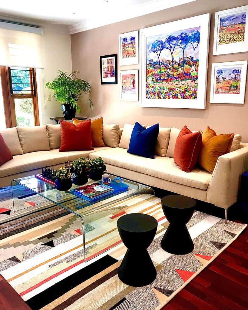 A cozy living room with a beige sectional sofa, colorful pillows, glass coffee table, and framed artwork on the wall