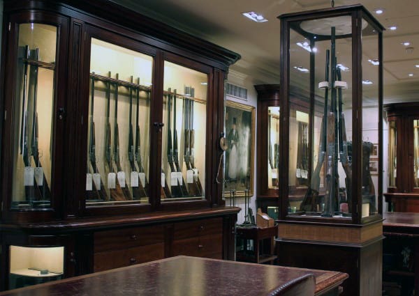 Sophisticated gun room featuring glass-encased collectors' firearms with elegant wooden cabinetry.