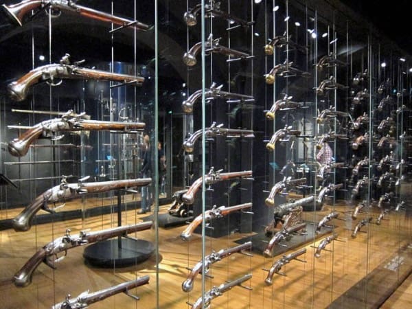Modern gun display featuring antique pistols elegantly mounted on transparent glass racks with ambient lighting.