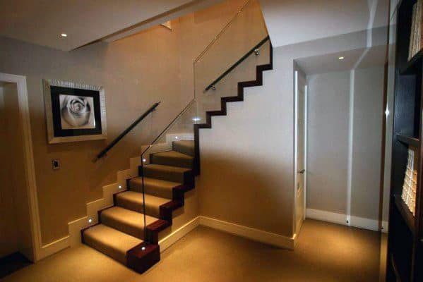 Carpeted staircase with glass railing and soft lighting in a contemporary home interior.