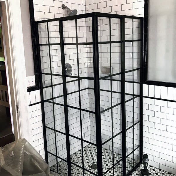 Corner shower with black-framed glass panels and white subway tiles, featuring a black and white mosaic floor design