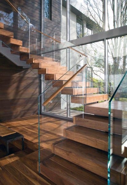 Modern staircase with glass railings, surrounded by large windows and bathed in natural light