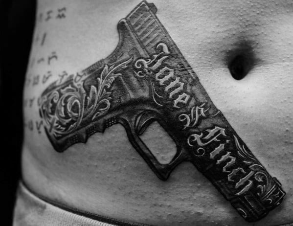Ornate black and grey tattoo of a Glock pistol on the stomach, featuring intricate floral engravings and the words "Jane Finch" in bold script.