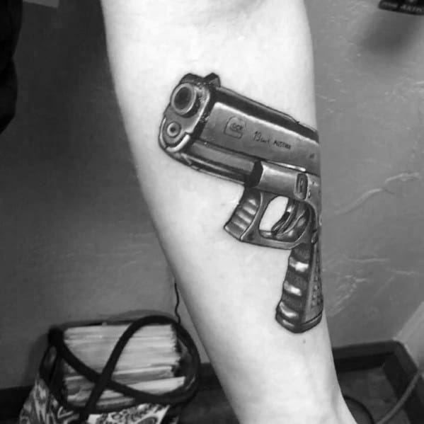 Realistic black and grey tattoo of a Glock pistol on the forearm, featuring detailed shading and perspective for a three-dimensional effect.