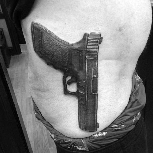 Realistic black and grey tattoo of a Glock pistol on the side of the torso, designed to appear as if the gun is holstered against the body.