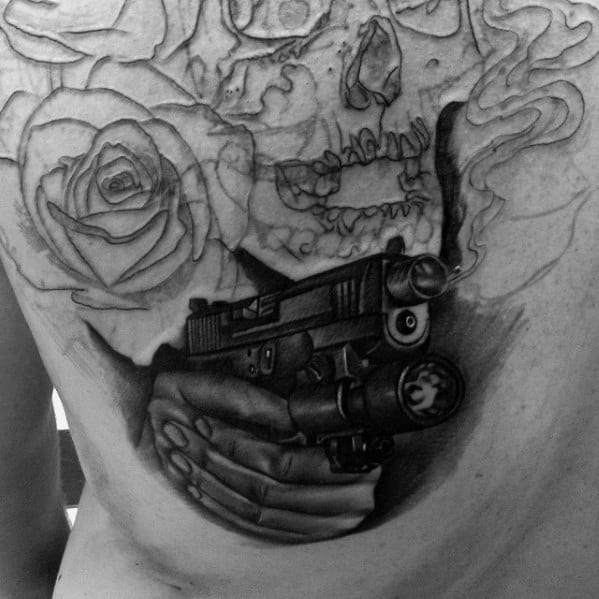 Realistic black and grey tattoo of a hand holding a Glock with a flashlight attachment, surrounded by a skull, roses, and smoke details.