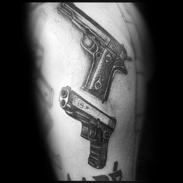 Black and grey tattoo of a Glock and a 1911 pistol on the upper arm, featuring detailed shading for a realistic and bold firearm design.