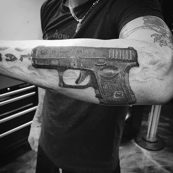 Realistic black and grey tattoo of a Glock 26 on the forearm, featuring fine shading and details to create a bold and three-dimensional effect.