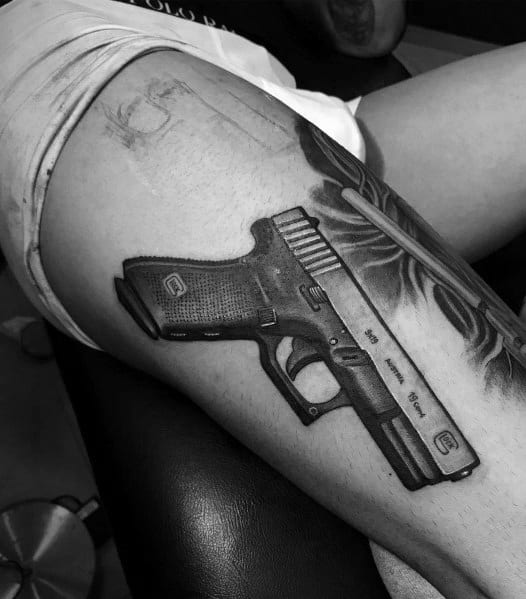 Realistic black and grey tattoo of a Glock pistol on the thigh, featuring detailed shading and depth for a three-dimensional and lifelike appearance.