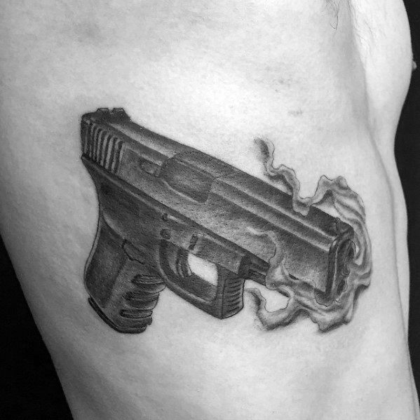 Realistic black and grey tattoo of a Glock pistol on the side of the body, featuring smoke details emerging from the barrel for a dynamic effect.