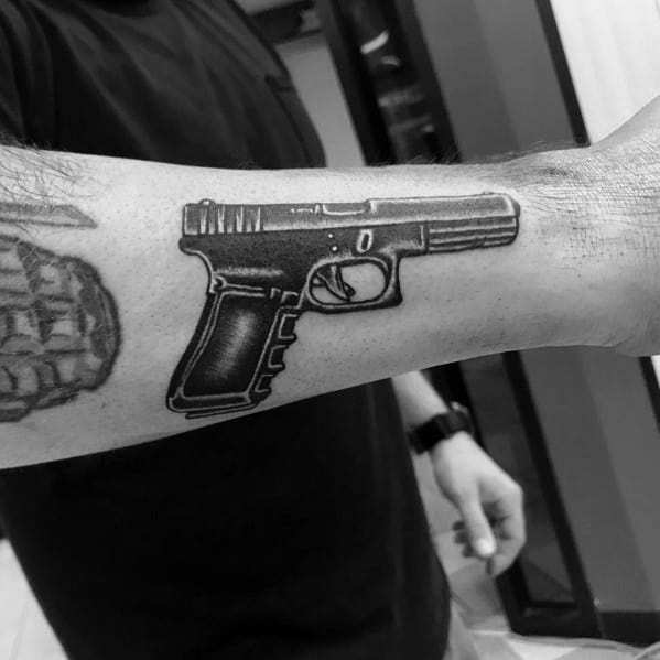 Black and grey tattoo of a Glock pistol on the forearm, featuring bold outlines and shading for a sharp, detailed, and realistic firearm design.