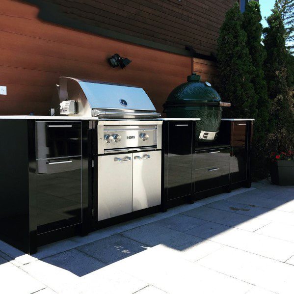 Built-in grill and green egg smoker sit on a patio with black cabinets in this outdoor kitchen