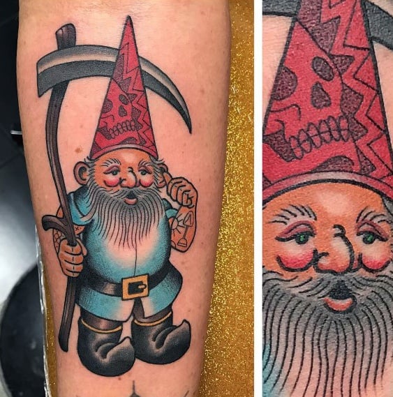 Tattoo of a mischievous gnome with a red skull-patterned hat, blue outfit, and black boots, holding a scythe with a playful smirk.