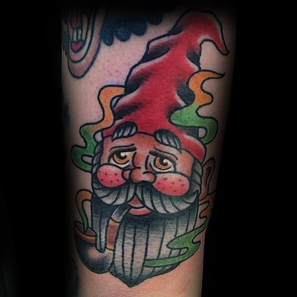 Tattoo of a floating gnome head with a red hat, bushy gray beard, and rosy cheeks, surrounded by colorful swirling smoke.