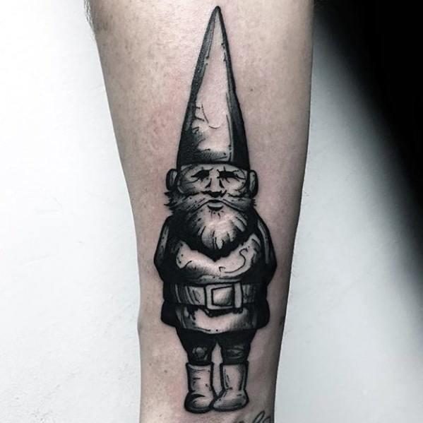 Black and white tattoo of a solemn gnome with a long pointed hat, bushy beard, and hands clasped, standing in a classic pose.