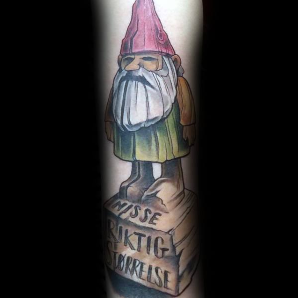 Tattoo of a gnome with a red hat, long white beard, and sunglasses, standing on a wooden block with the inscription "NISSE RIKTIG STØRRELSE."