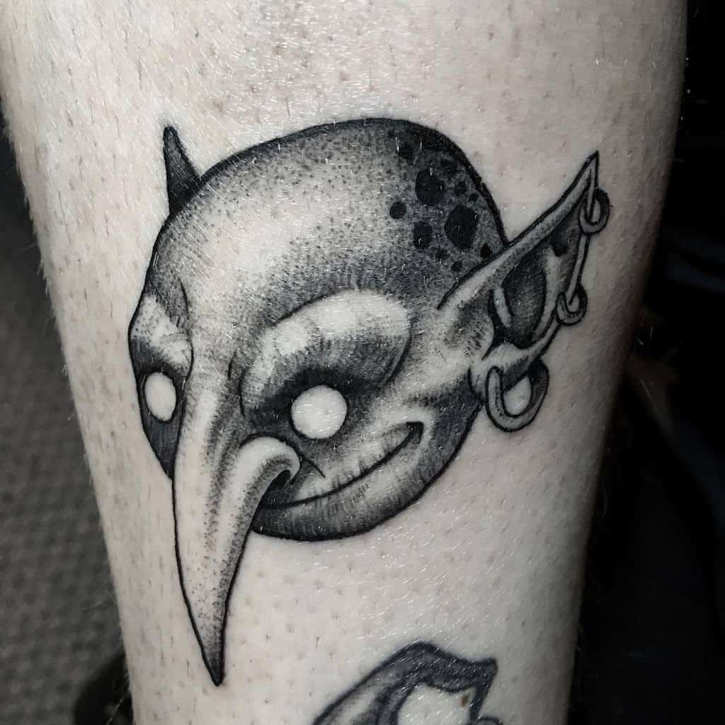 Black-and-gray goblin head tattoo with exaggerated features, piercings, and a mischievous expression