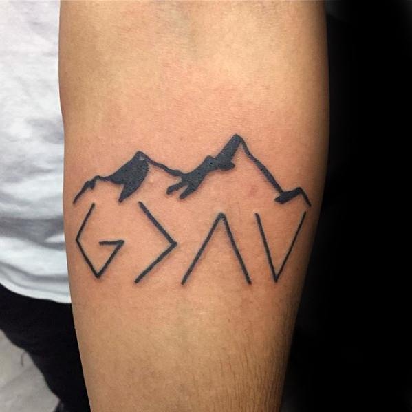 Forearm tattoo featuring "God is greater than the highs and lows" symbol with bold mountain outline design