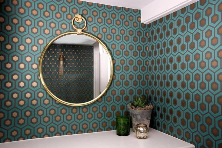 Bathroom with teal and gold geometric wallpaper, round gold mirror, and small decor.
