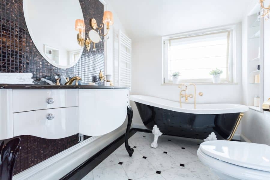 Elegant black and white bathroom with gold accents, clawfoot tub, and mosaic wall tiles.