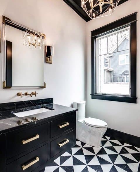 Elegant bathroom with black vanity, geometric tile floor, gold fixtures, and chandelier.