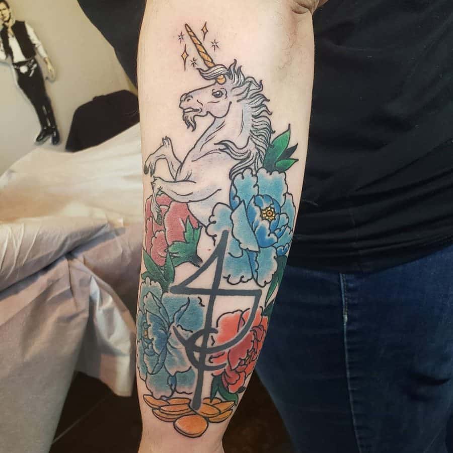 Bold and colorful forearm tattoo of a rearing unicorn with a golden horn, surrounded by vibrant peonies and a large astrological symbol.