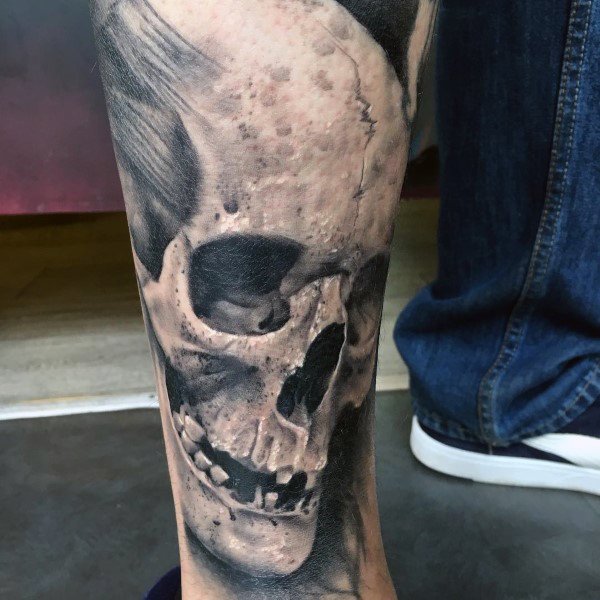 Realistic skull tattoo on the lower leg in black and grey, featuring high contrast shading and fine bone details for a 3D effect.