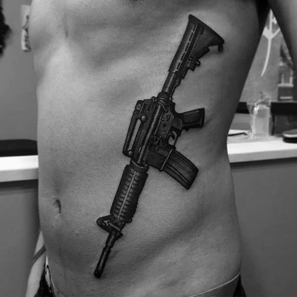 Large black and grey AR-15 tattoo on the ribcage, featuring intricate details and bold shading, symbolizing strength, resilience, and firearm appreciation.
