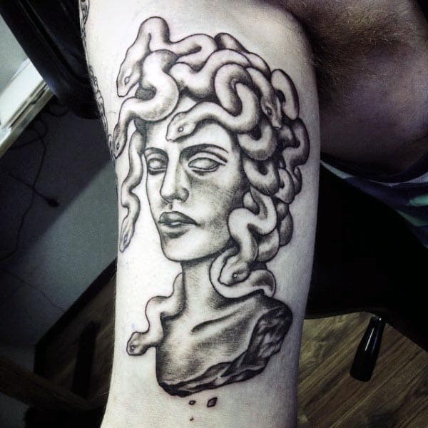 Black and grey tattoo of Medusa in a classical bust style, with detailed snakes in her hair and smooth shading on the upper arm