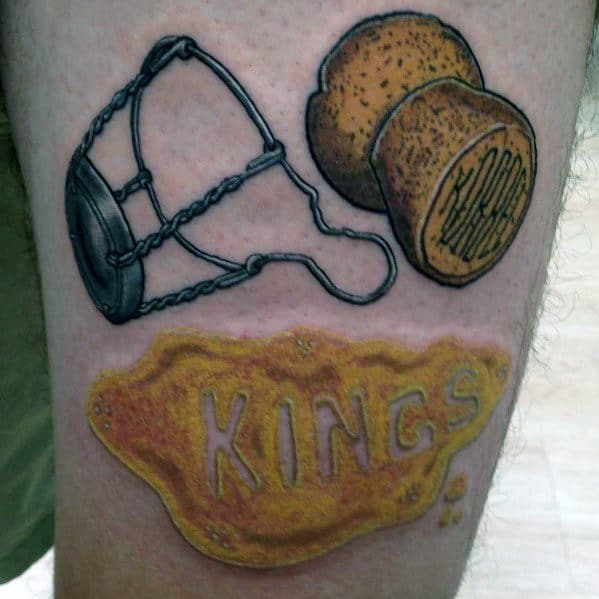 Color tattoo featuring a champagne cork, wire cage, and a gold label with the word "KINGS" in bold letters.