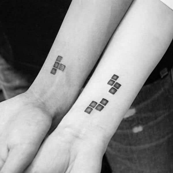 Minimalist matching tattoos of Tetris blocks on wrists, symbolizing how two pieces fit perfectly together in love and life.