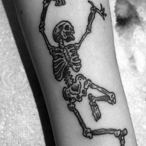 Dancing skeleton tattoo with raised arms and a playful pose, featuring bold black ink and fine details for a striking and lively design.