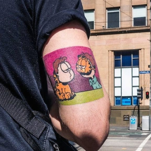Colorful Garfield tattoo featuring a comic-style scene with Jon, set in a vibrant background—bold and nostalgic design for fans.