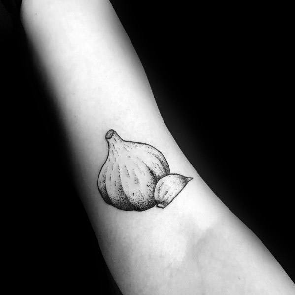 Minimalist garlic tattoo on the forearm with fine dotwork shading, featuring a whole bulb and a single clove for a simple botanical design.