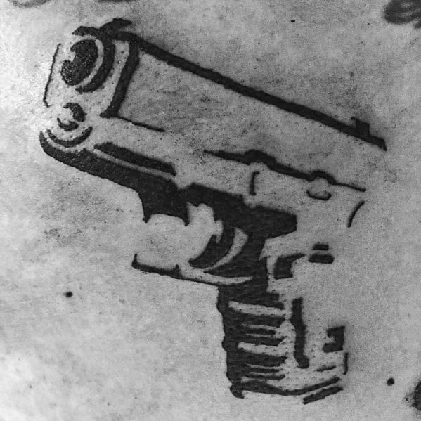Minimalist black ink tattoo of a Glock pistol, featuring a bold stencil-like design with rough edges for a raw and edgy aesthetic.