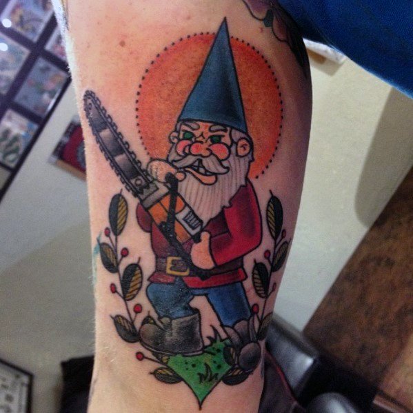 Tattoo of a fierce gnome with a blue hat and red coat, wielding a chainsaw, standing on grass with a bold orange sunburst background.
