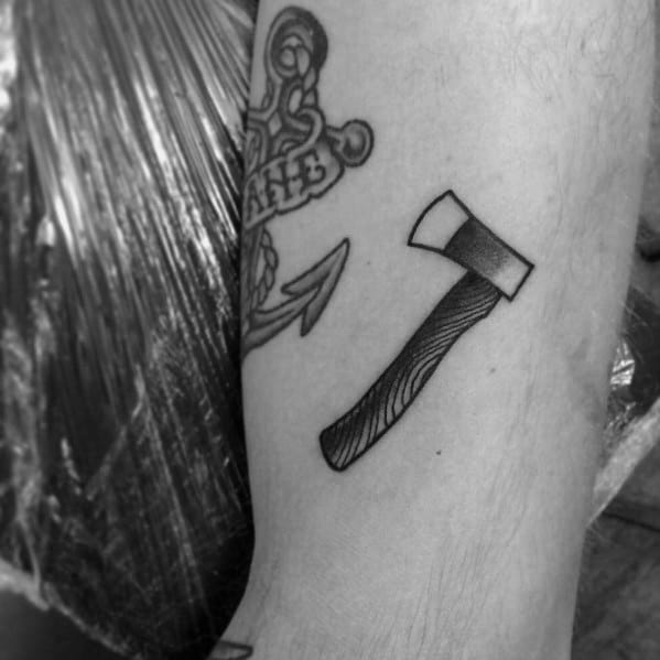 Small black and grey hatchet tattoo on the forearm with a textured wooden handle and a shaded blade, designed with clean, bold lines.