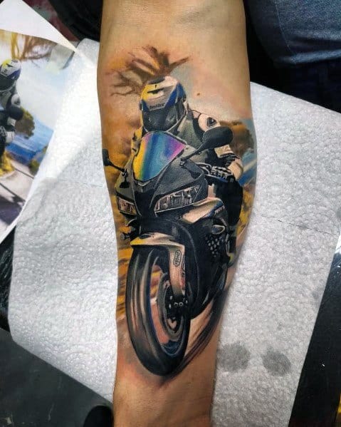 Realistic Honda sportbike tattoo on a man's forearm, featuring a dynamic rider in motion with vibrant colors and detailed shading.