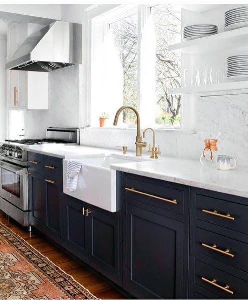 Black kitchen cabinets with gold hardware, farmhouse sink, white marble countertop, and shelves.
