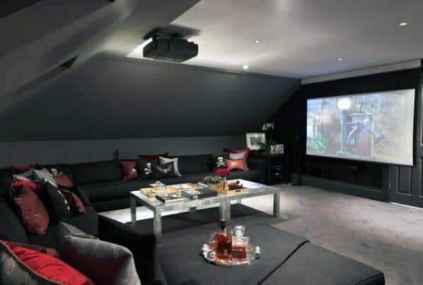 Attic home theater with dark seating, red accents, coffee table, and ceiling-mounted projector.