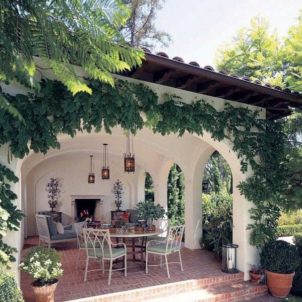 Charming patio with vine-covered arches, brick accents, outdoor seating, and a fireplace