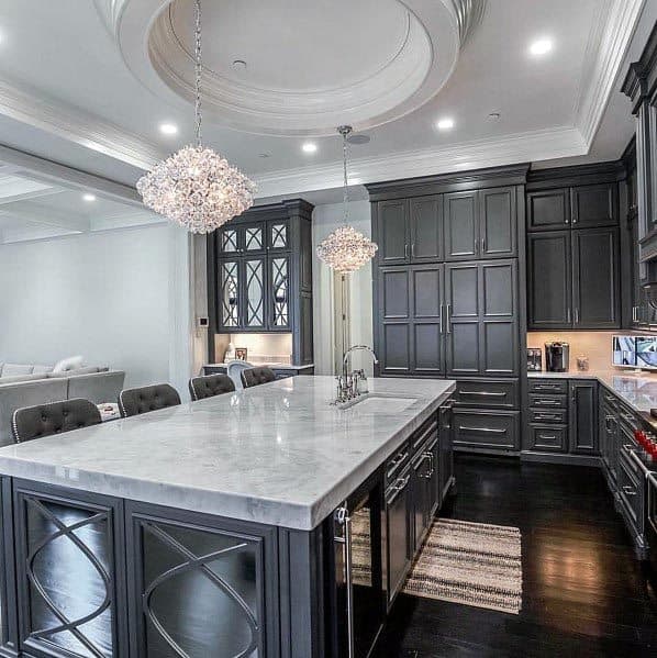 Dark grey kitchen with marble island, crystal chandeliers, and elegant cabinetry design.