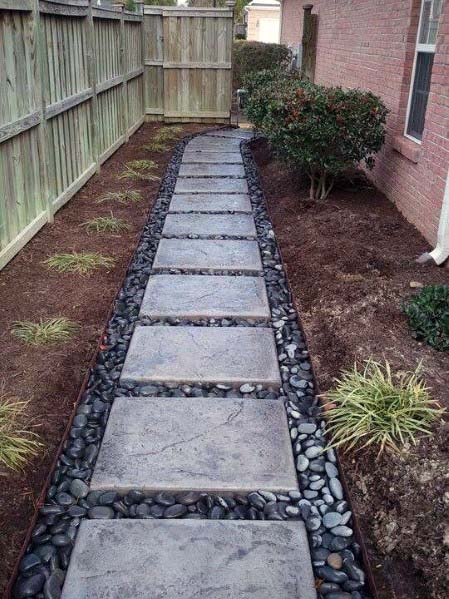 Stepping stone walkway bordered by river rocks and grass, creating a clean and simple path along a wooden fence