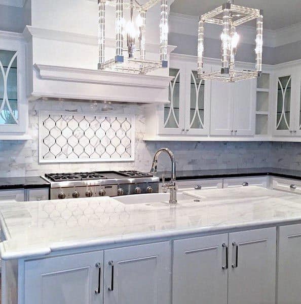 White kitchen with marble island, crystal pendant lights, and decorative backsplash.