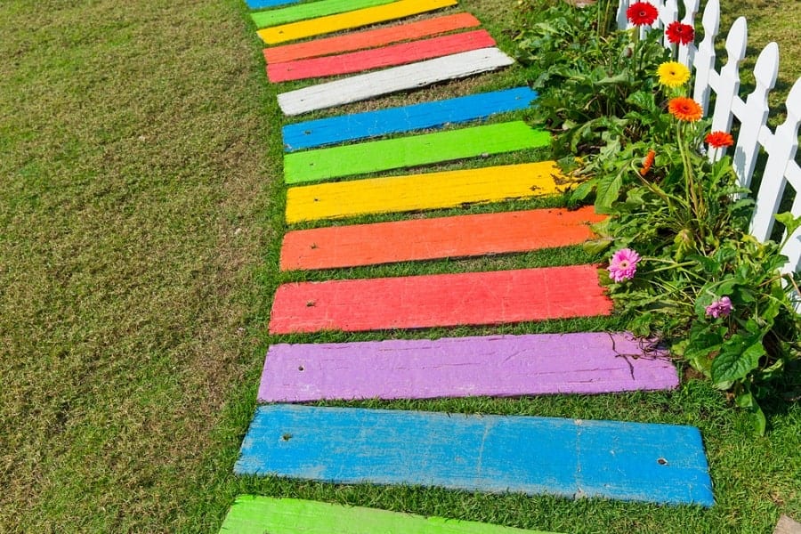 Colorful wooden walkway with flowers and white picket fence on a grassy lawn
