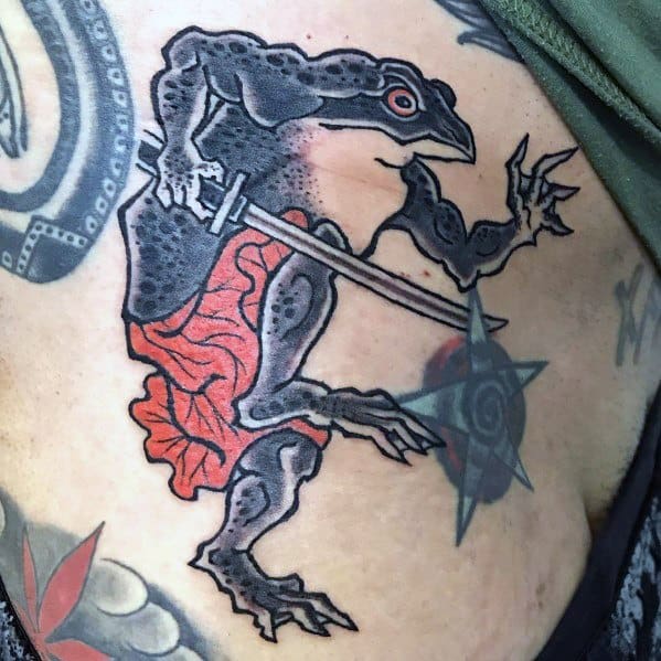 Japanese-style tattoo of a black warrior frog wielding a sword and shuriken, dressed in a red loincloth, symbolizing strength and agility.