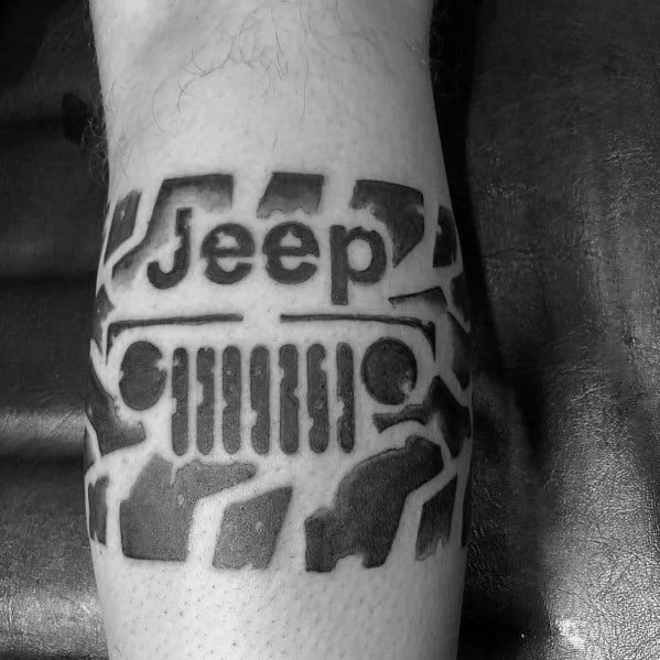 Bold black Jeep tattoo on the forearm, featuring the Jeep grille, headlights, and logo integrated with rugged tire tracks for a dynamic design.