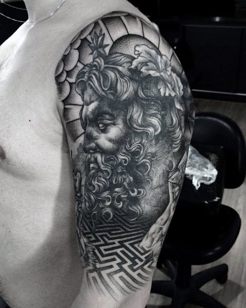 Realistic black and grey tattoo on a man's upper arm, featuring a detailed Greek god portrait above a geometric labyrinth design.