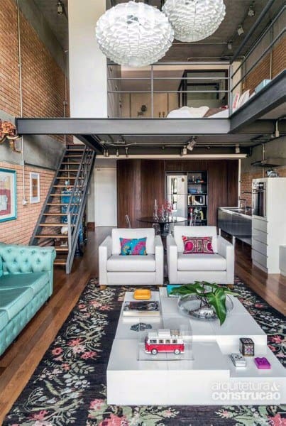 Colorful loft with brick walls, floral rug, modern furniture, and mezzanine bedroom area.